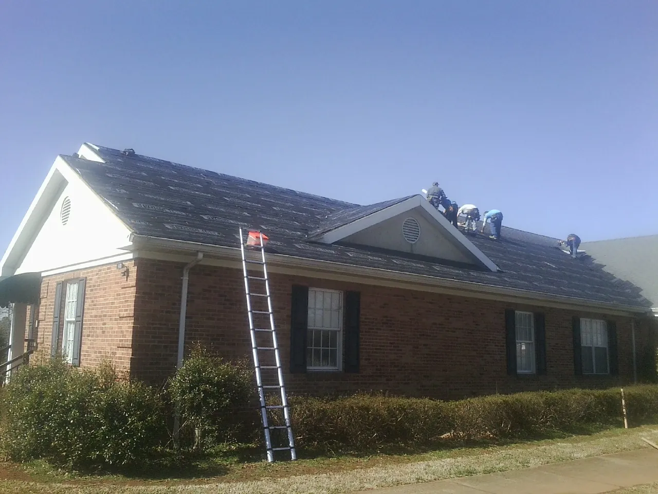 Crew tearing shingles off a brick ranch roof with a ladder set — Metal Roof Repair work by our crew in Newark